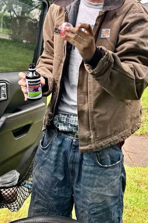 A man in a brown jacket holding a bottle of beer.