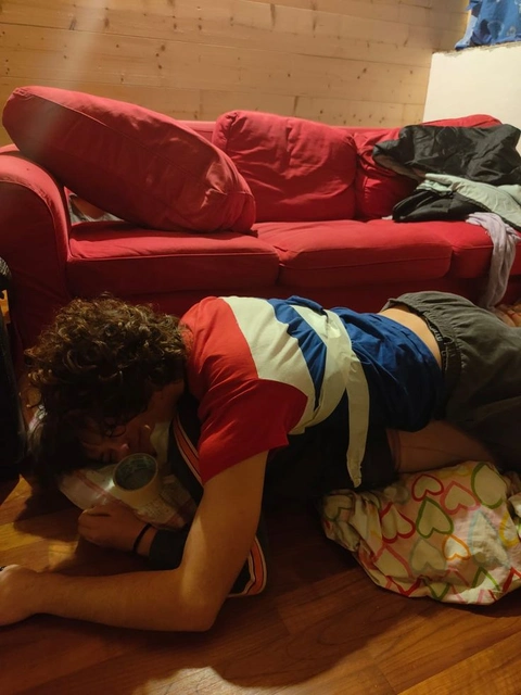 A man laying on the floor in front of a red couch.