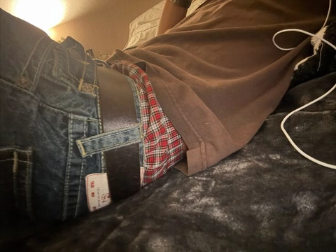 A pair of jeans and a brown jacket are stacked on top of each other.