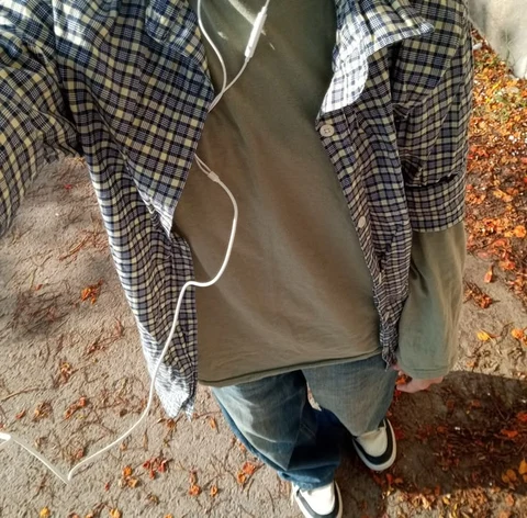 A person wearing a plaid shirt and jeans standing in front of a wall.