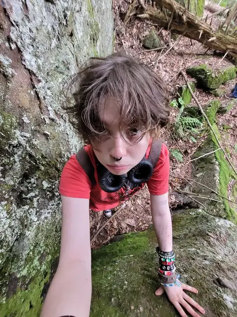 A young boy standing in front of a tree covered in moss.