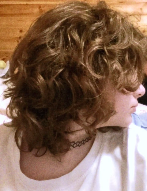 A woman with curly hair is reflected in a mirror.