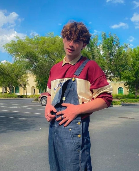 A man in overalls standing in the middle of a parking lot.