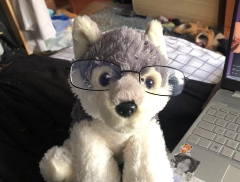 A stuffed animal wearing glasses sitting in front of a laptop.