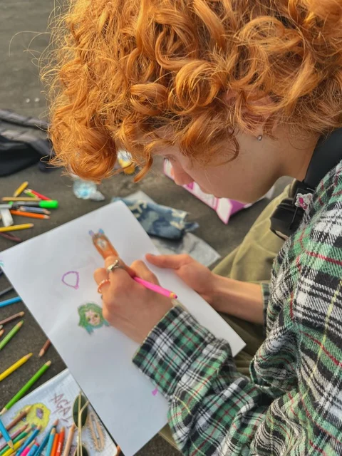 A young girl with curly hair drawing on a piece of paper.
