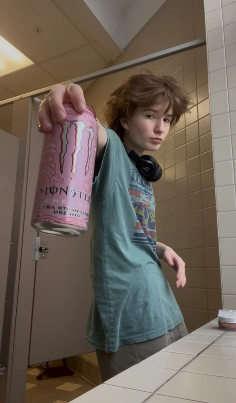 A woman holding a can of Monster energy drink in front of a mirror.