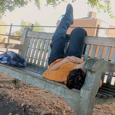 A couple of people laying on top of a wooden bench.