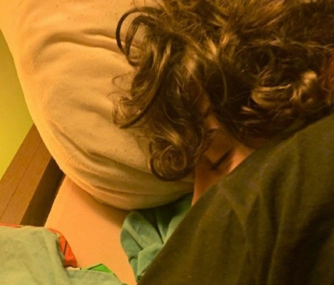 A woman with long curly hair laying on a bed.