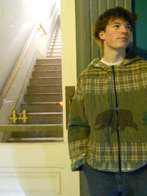 A young man standing in front of a door with a number 44 on it.