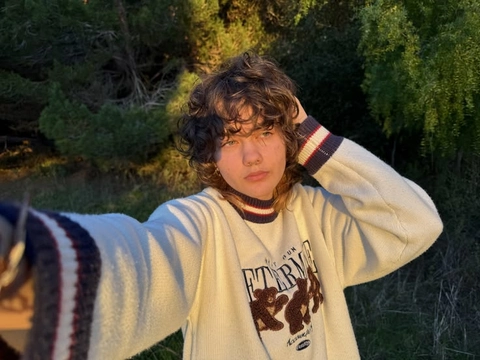 A young boy in a sweater standing in front of a forest.