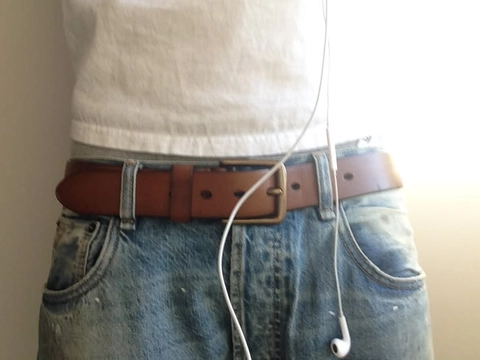 A pair of jeans with a brown belt and earphones attached to it.