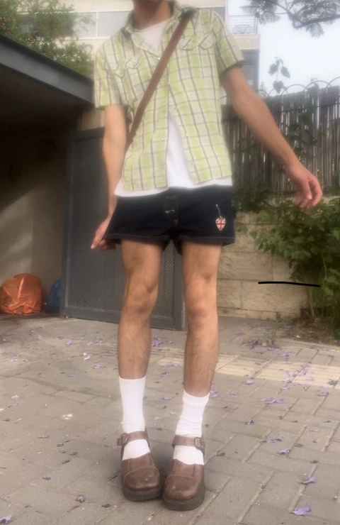 A man in shorts and a plaid shirt is standing in front of a fence.