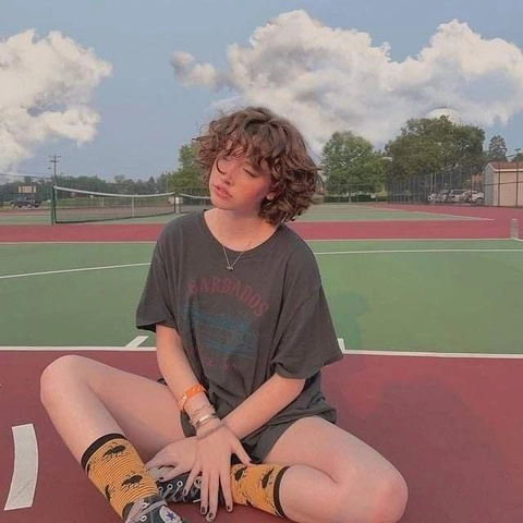 A young man sitting on a tennis court with his legs crossed.