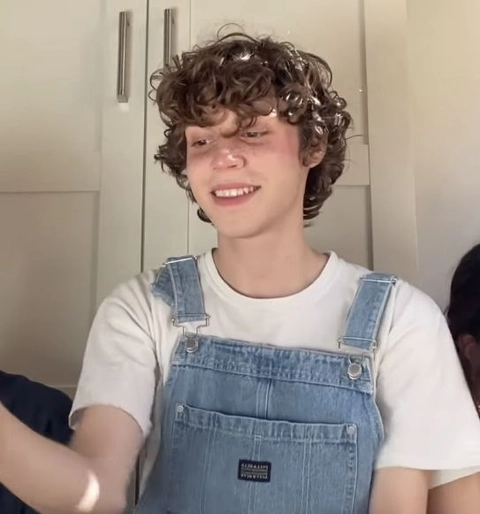 A young boy with curly hair wearing overalls and a white shirt.