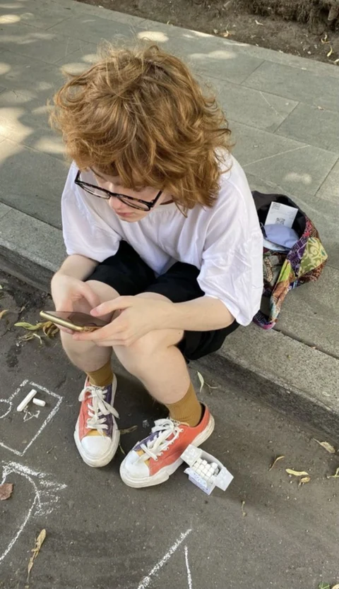 A young boy sitting on a bench looking at his cell phone.
