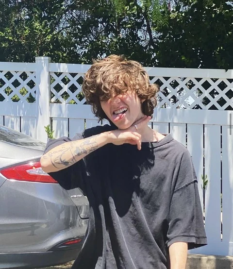 A man with curly hair standing in front of a white fence.
