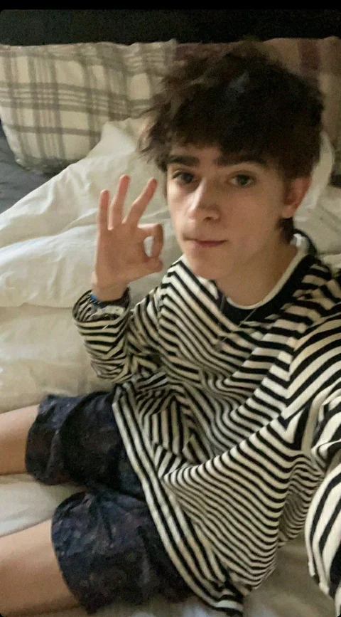 A young man sitting on top of a bed with his hands up.