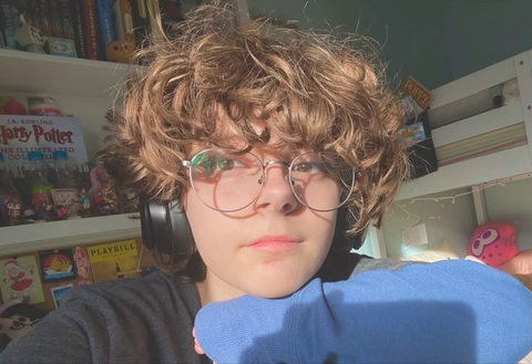 A young boy wearing glasses and a wig with curly hair.