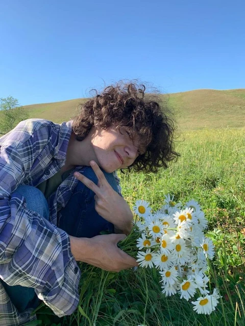 A woman laying in a field of daisies with her hands on her face.