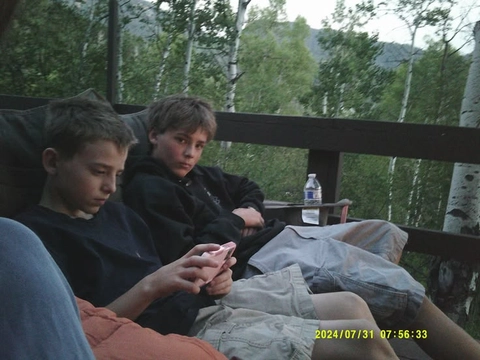 A group of young people sitting on a bench looking at their cell phones.