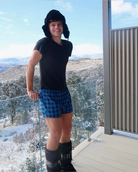 A man in a black shirt and blue shorts standing on a balcony.