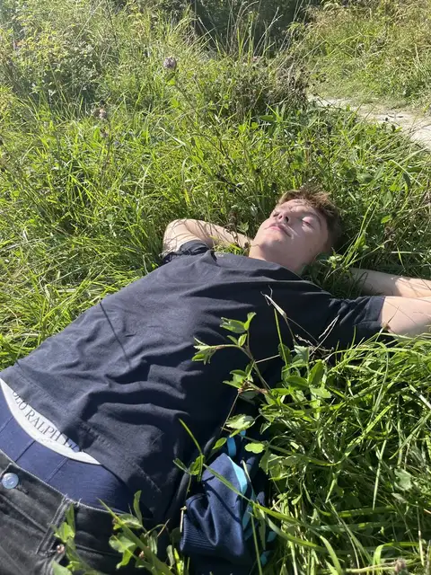 A man laying in the grass with his head in his hands.