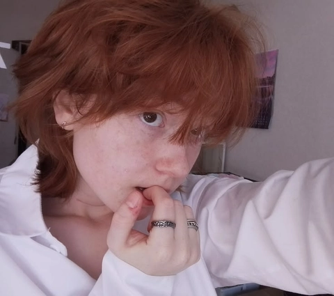 A woman with red hair and a white shirt is making a funny face.