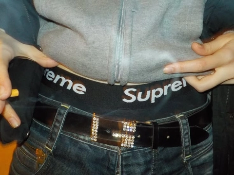 A woman wearing a black belt with the word Supreme on it.