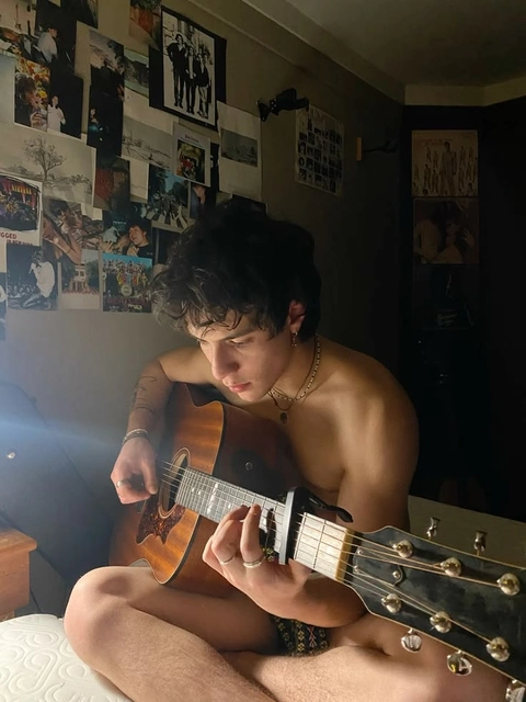 A man sitting on a bed playing a guitar.
