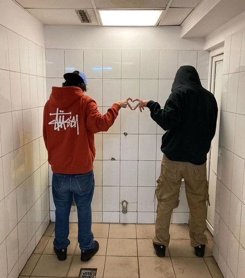 A couple of people standing in a bathroom making a heart shape.