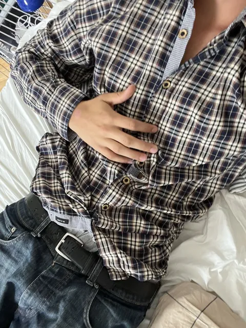 A man wearing a plaid shirt and jeans on a bed.