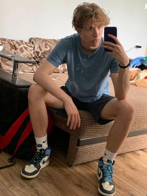 A young man sitting on a couch taking a selfie.
