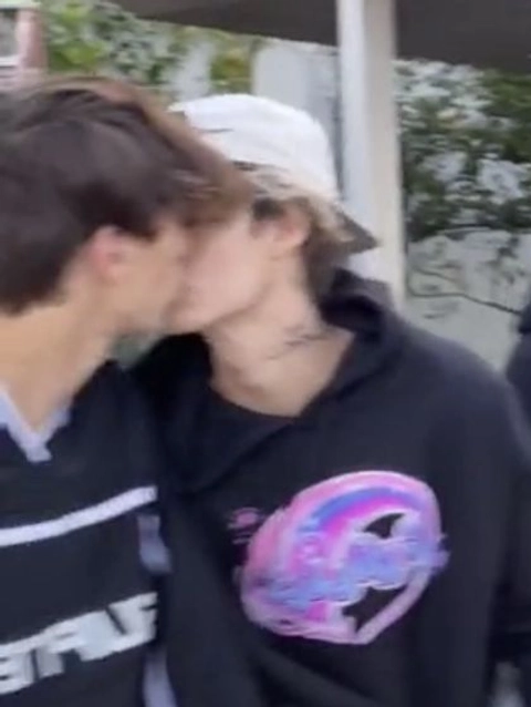 A couple of young men kissing each other in front of a fence.