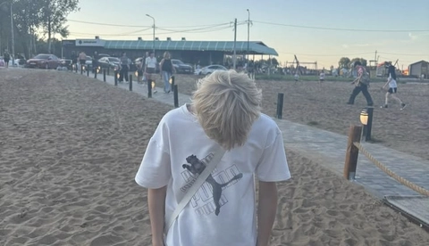 A man with long blonde hair standing in the sand.