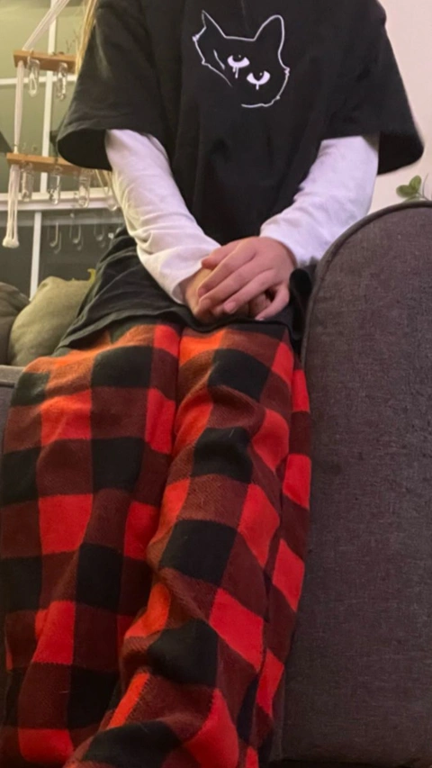 A person sitting on a couch wearing a black shirt and red plaid pants.