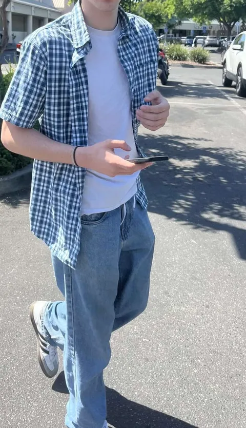A man in a plaid shirt and jeans is walking down the street.