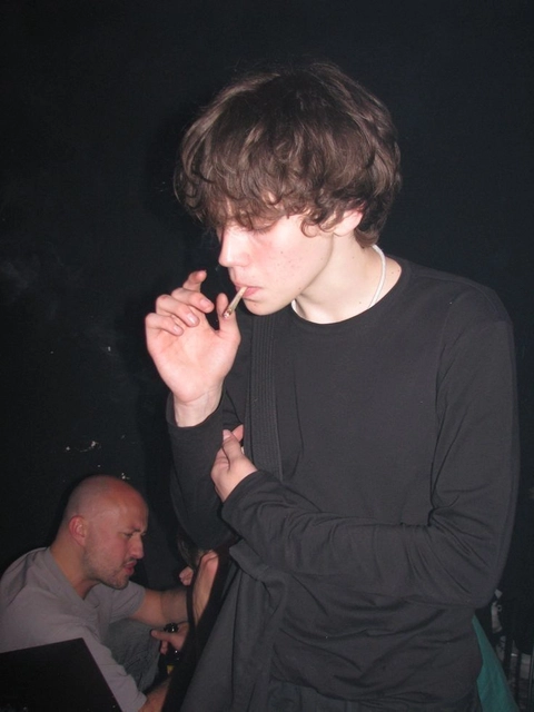 A young man smoking a cigarette in front of a group of people.