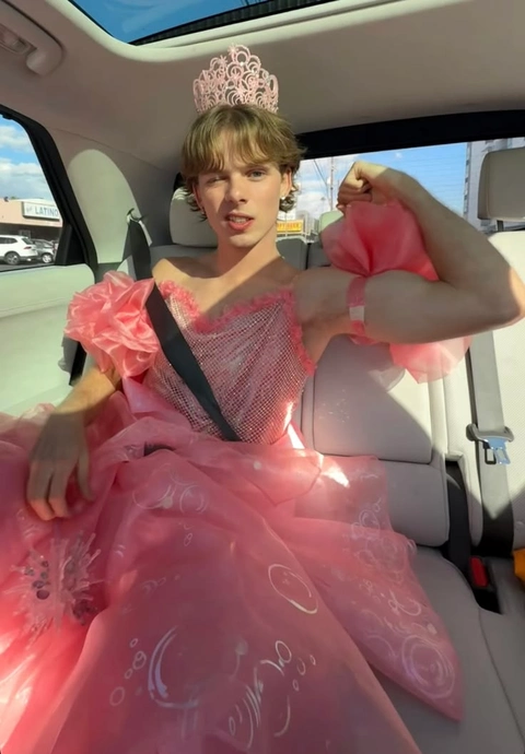 A woman in a pink dress sitting in the back seat of a car.