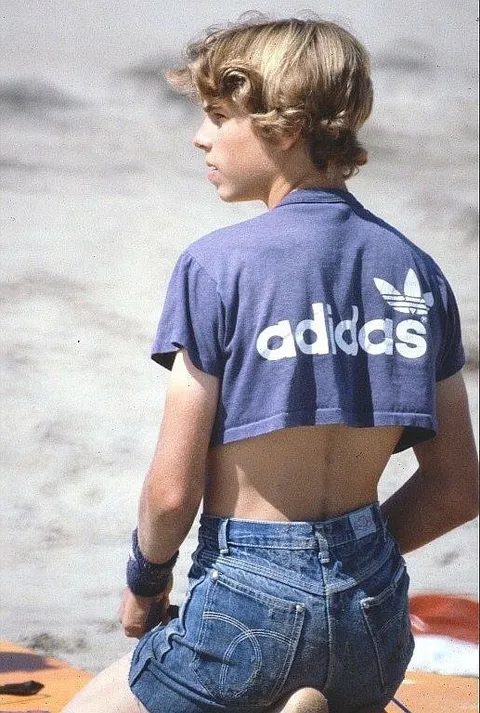 A young boy wearing a purple adidas shirt and denim shorts.