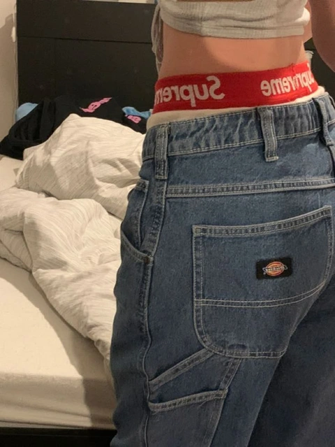 A pair of jeans with a red waistband on a bed.