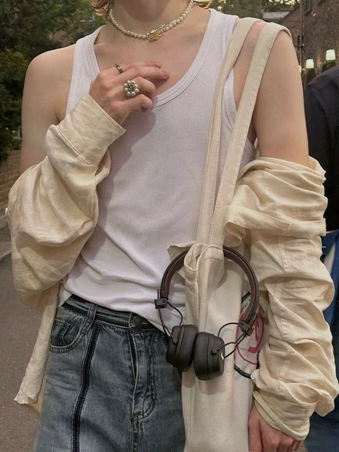 A woman wearing a white tank top and a pair of headphones.