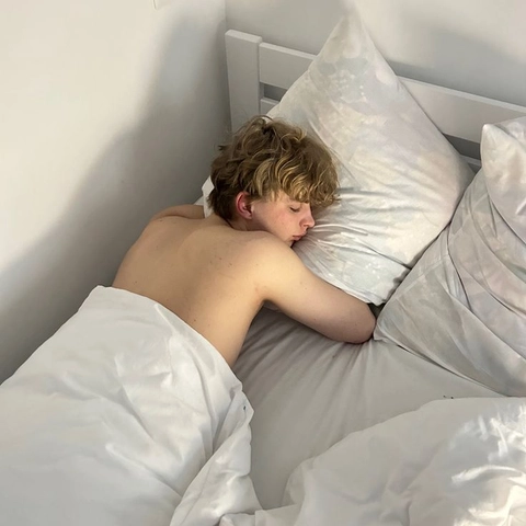 A young boy laying in bed with pillows on his head.