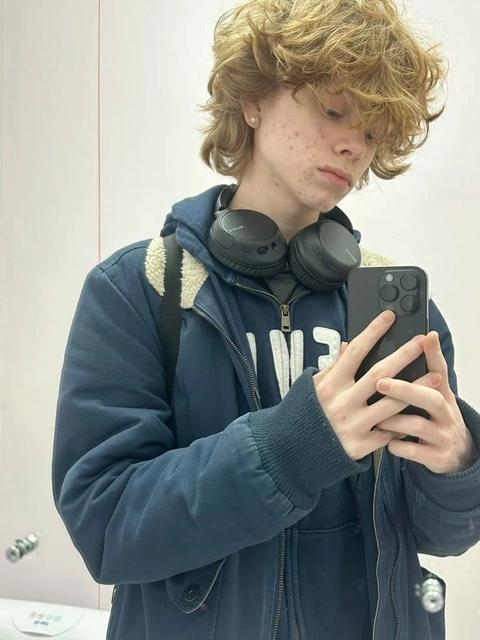 A young man with curly hair holding a cell phone.