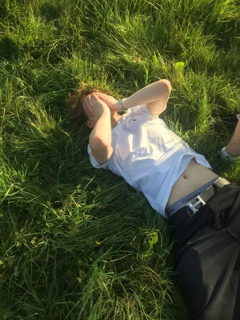 A man laying in the grass with his hands on his face.
