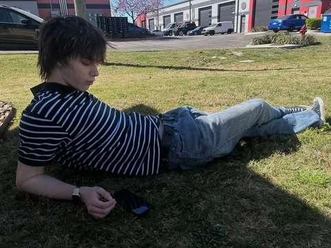 A man laying on the grass with his cell phone.