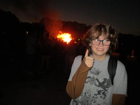 A young boy giving a thumbs up in front of a fire.