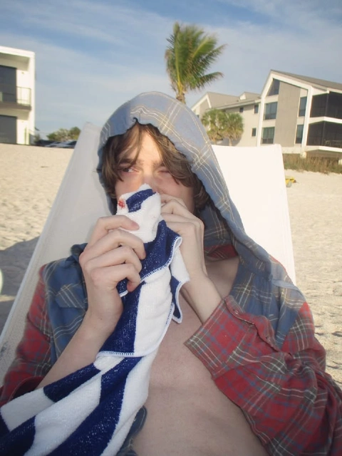A young man sitting in a hammock on the beach.