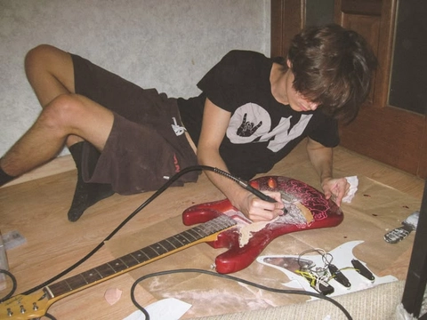A young man sitting on the floor playing a guitar.