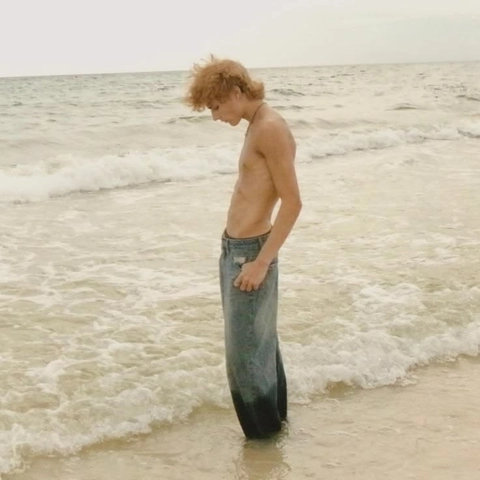 A shirtless man standing in the ocean with his hands on his hips.