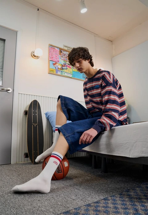 A man sitting on a bed with a basketball in his feet.